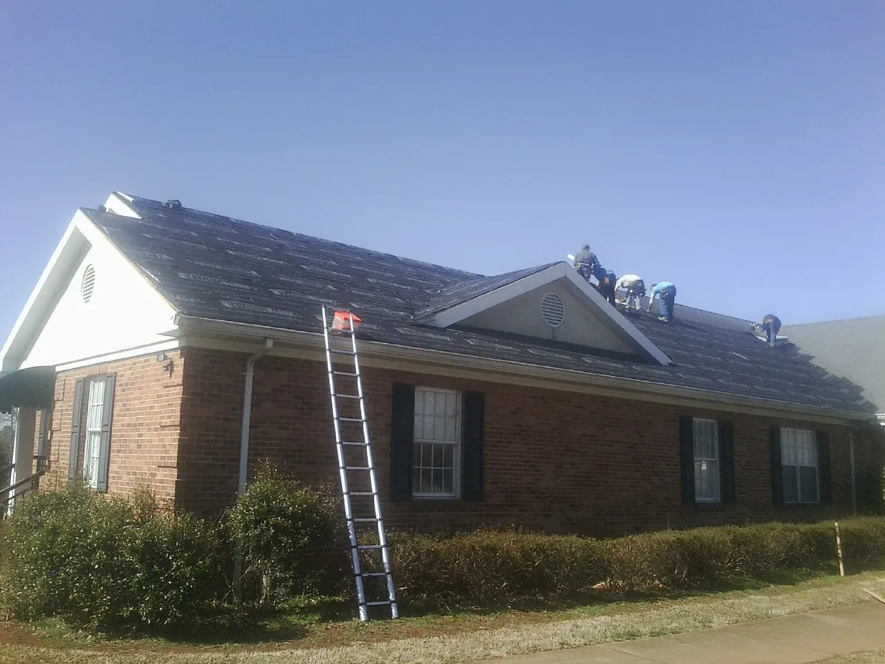 Crew tearing shingles off a brick ranch roof with a ladder set — Emergency Roof Repair work by our crew in Deerfield