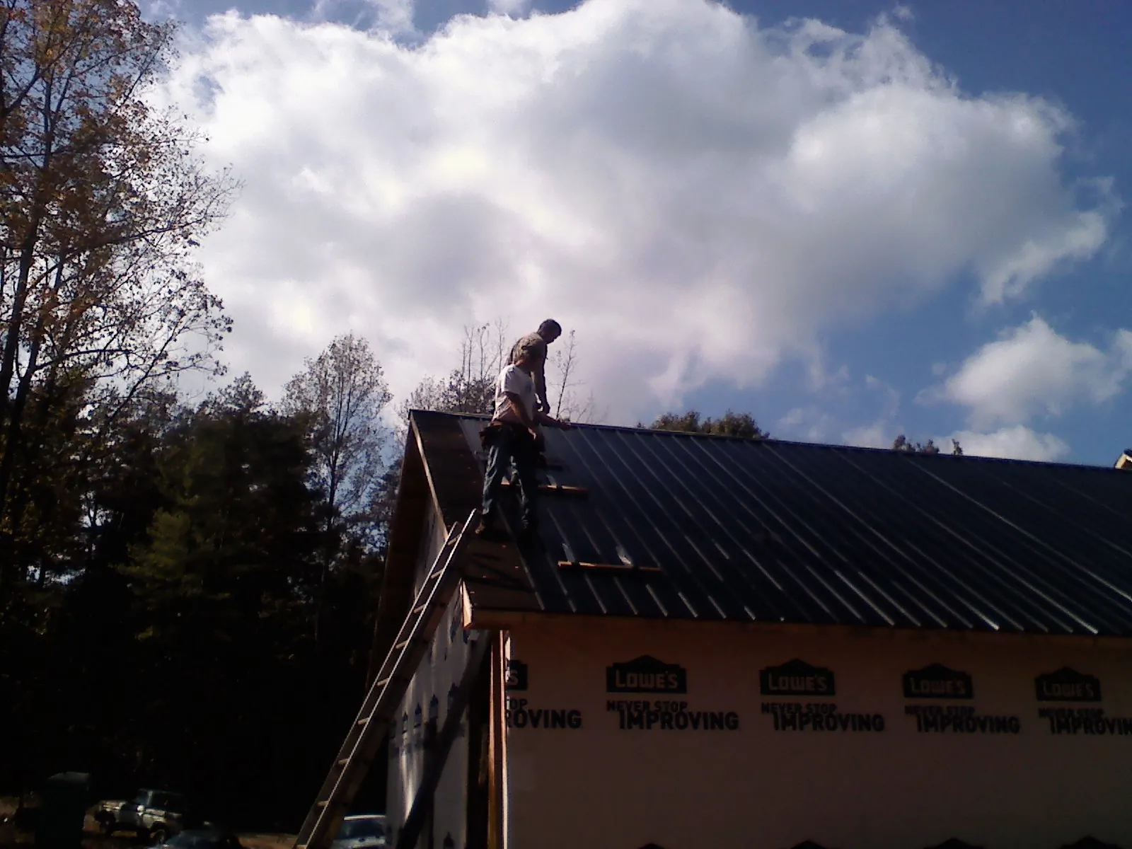 Roofer fastening dark metal panels high against a cloudy sky, from a Roof Inspection job in Deerfield