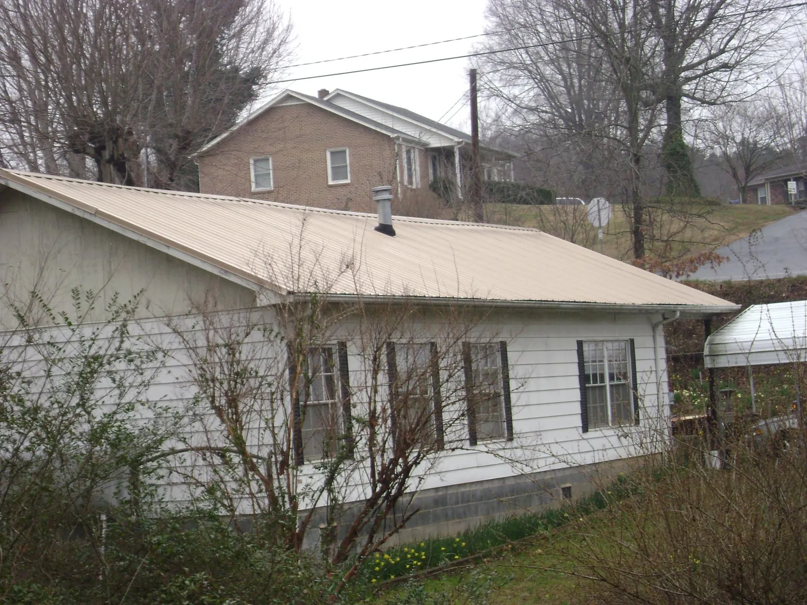 Tan metal roof on a white sided house set into a hillside — Commercial Roofing by Roofing Brothers in Deerfield
